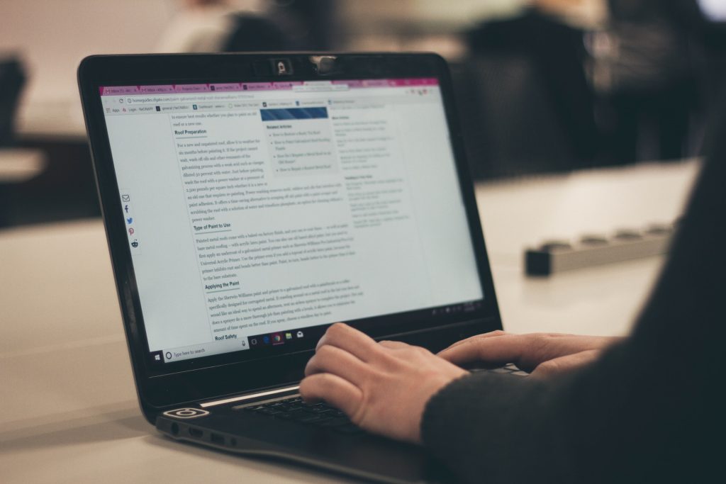 Un PC portable de couleur noire ouvert sur un bureau avec une personne en train de rédiger du contenu