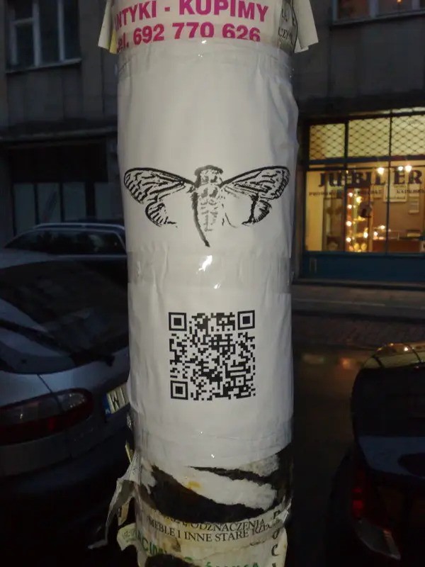 Un poteau sur lequel est scotché le logo Cicada 3301 ainsi qu'un QR code.