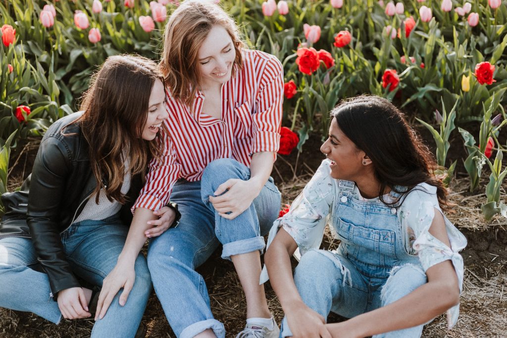 Trois jeunes femmes assises à côté de fleurs sont en train de discuter.