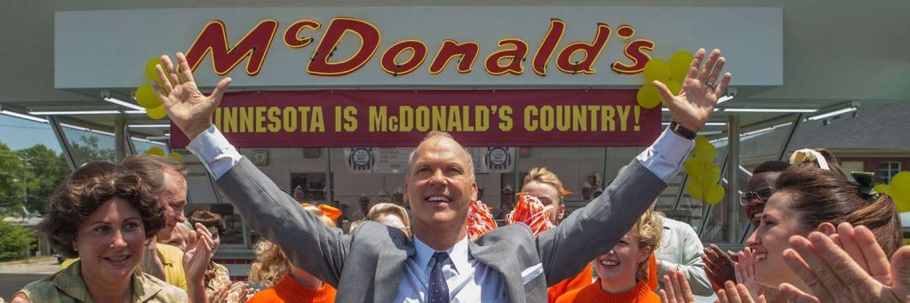 Photo turée du film Le Fondateur montrant Michael Keaton les bras levés devant un restaurant McDonald's
