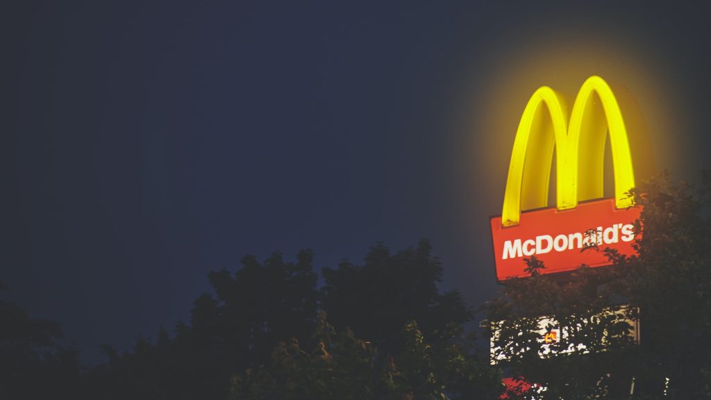 Photo nocturne d'un panneau Mc Donald's avec les arches dorées qui brillent dans la nuit.