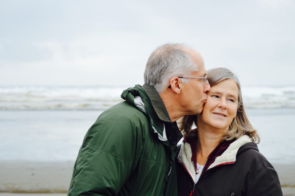 Un couple de personnes âgées s'embrasse sur une plage sous un ciel gris.