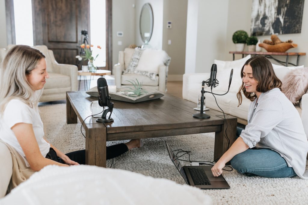 Deux jeunes femmes enregistrent un podcast en étant assise par terre et avec les micros posés sur une table basse