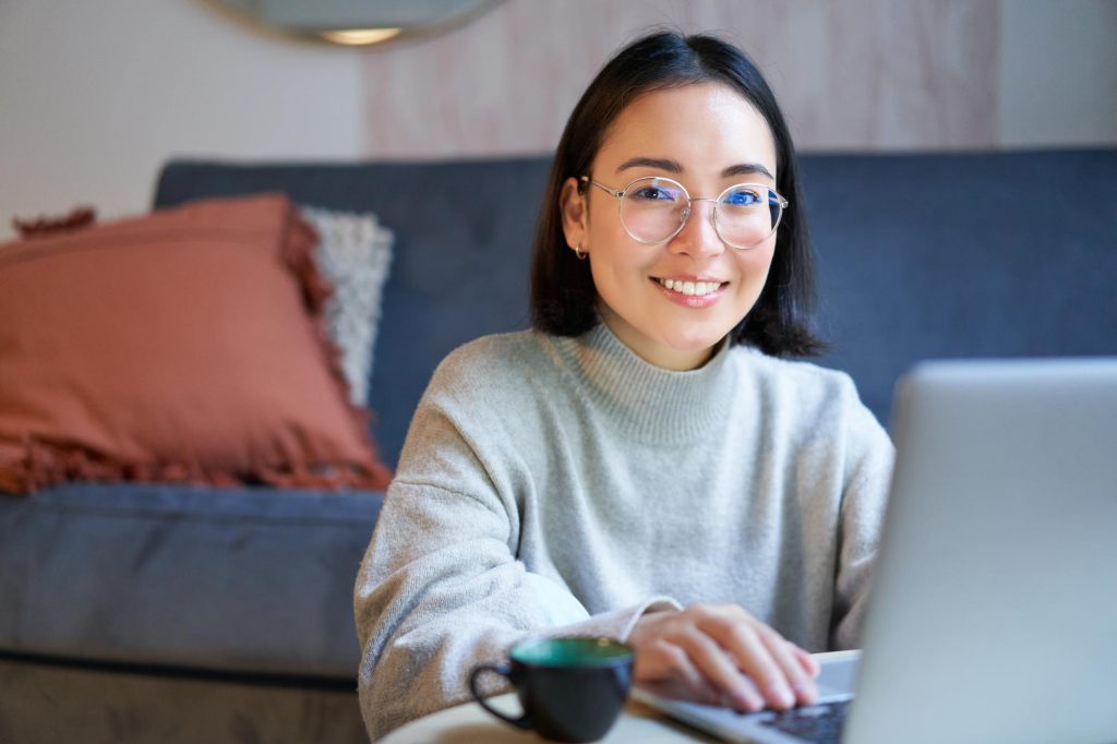 Une jeune femme souriante est en train d'utiliser son ordinateur portable.