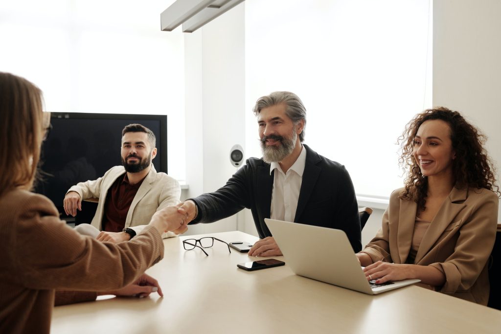 Une femme et un homme se serrent la main par dessus une table sous les yeux d'autres collaborateurs lors d'un entretien d'embauche