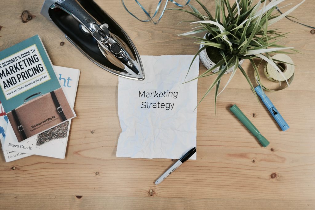 Une feuille de papier posée sur une table avec les mots Marketing Strategy écrits dessus. Un fer à repasser et des feutres sont également sur la table.